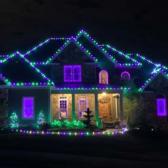 A two-story home outlined in purple and green lights along every roofline and window
